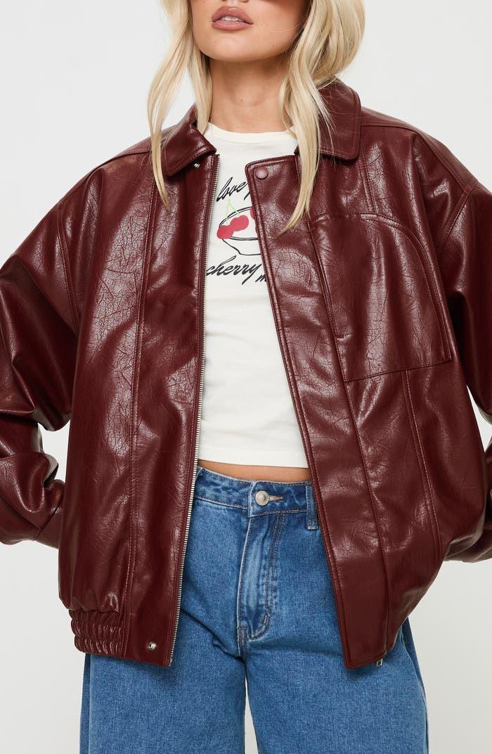 Woman wearing a crimson boxy faux leather jacket with drop shoulders and blue jeans