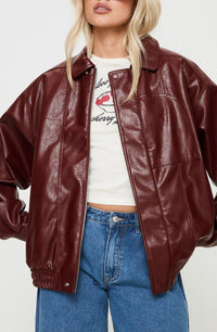 Woman wearing a crimson boxy faux leather jacket with drop shoulders and blue jeans