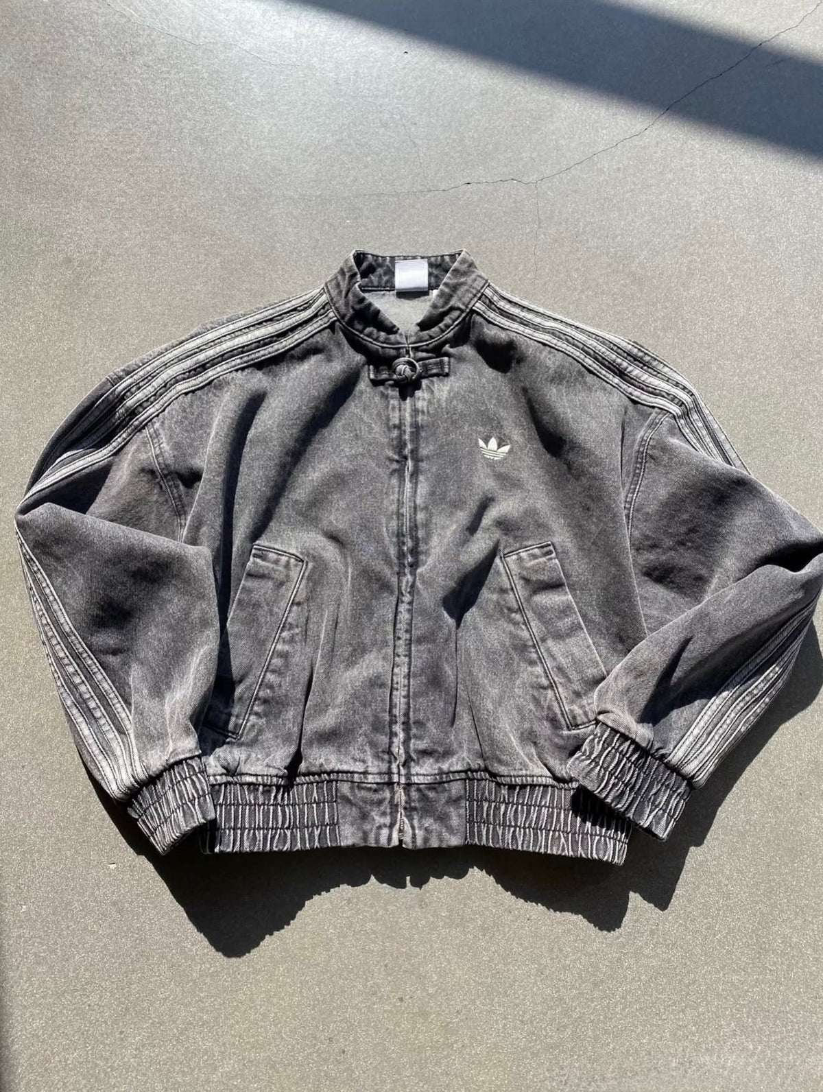 Black denim jacket with Adidas logo on a gray surface