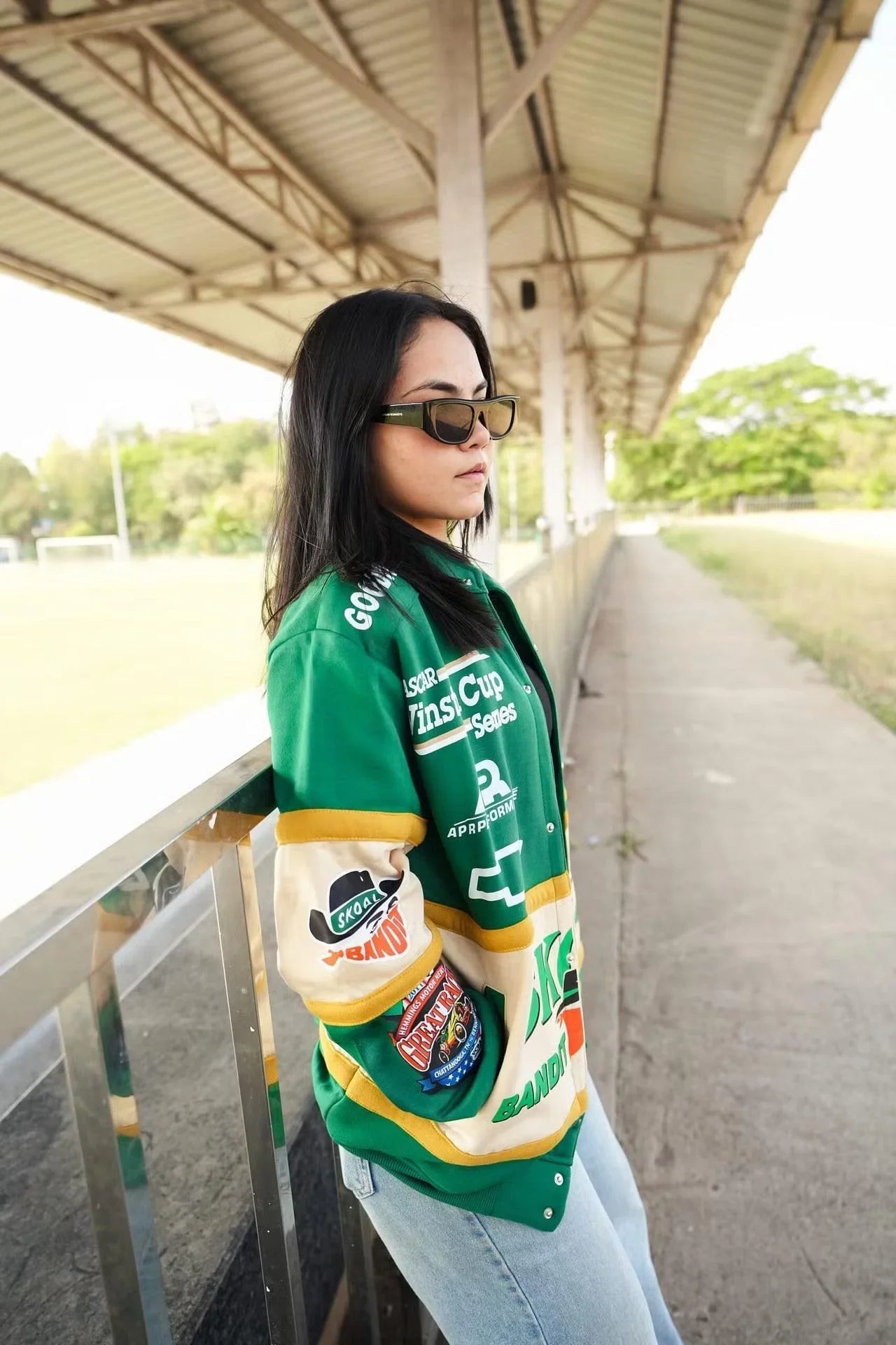 Woman in green vintage racing patch jacket with zipper, standing outdoors in streetwear style