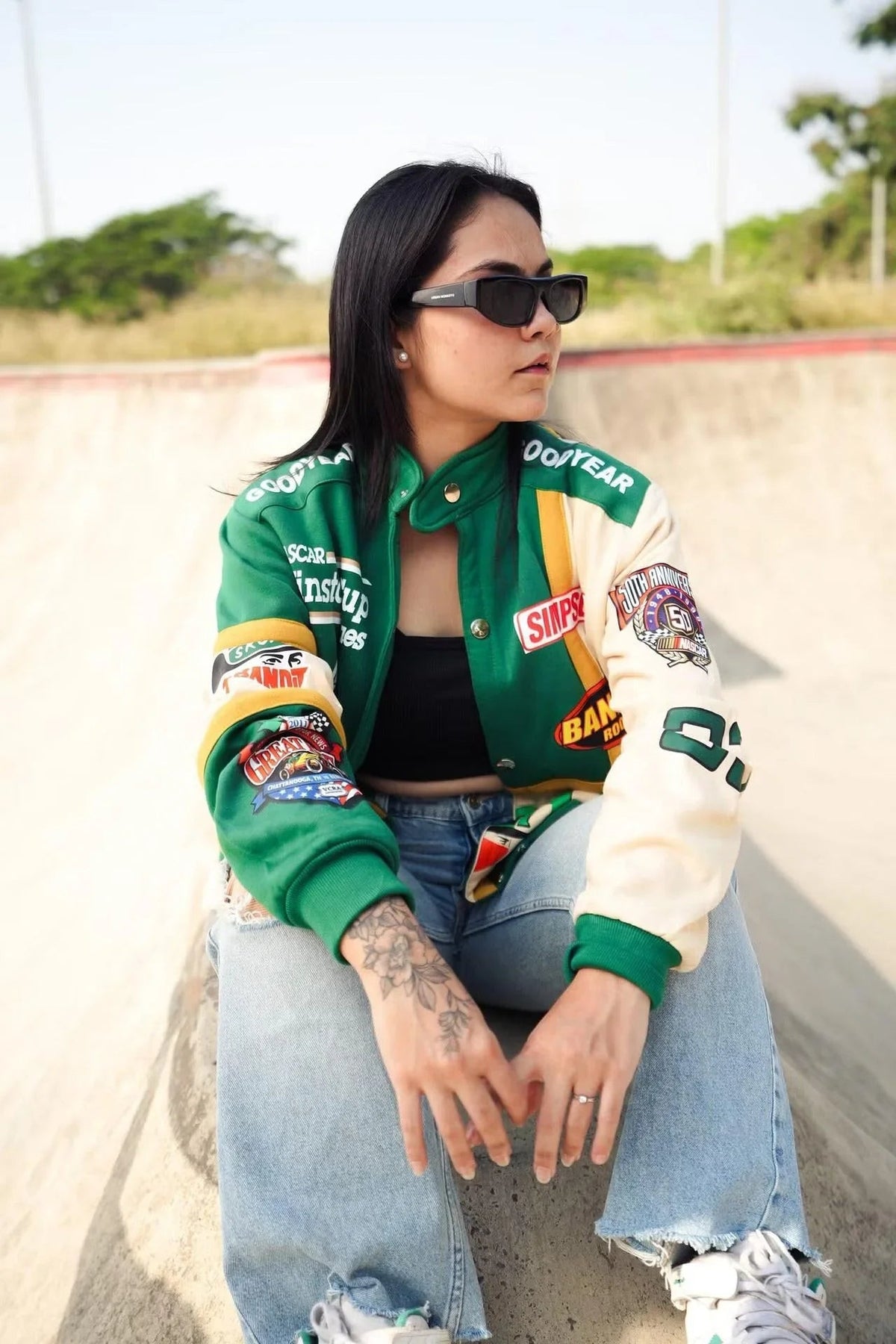 Model in oversized racing jacket, streetwear jeans, and sunglasses at skatepark