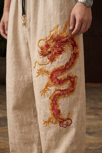 Detail shot of the elasticated drawstring waistband and metal toggles on beige wide-leg Chinese dragon pants styled with a red shirt.