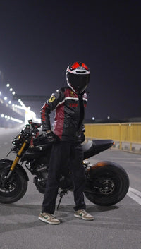 Motorcyclist in reinforced shoulder streetwear jacket and helmet posing by black motorcycle at night